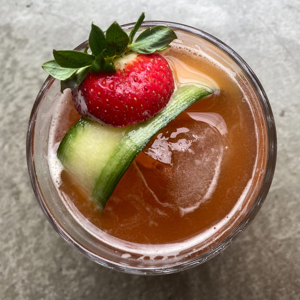 AnQi Bistro's Asian-fusion cocktail, garnished with a strawberry, cucumber slice, and ice.