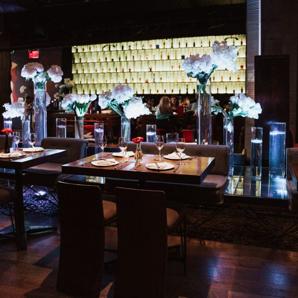 AnQi Bistro's dimly lit dining room with set tables, white floral arrangements, and a glowing bar.