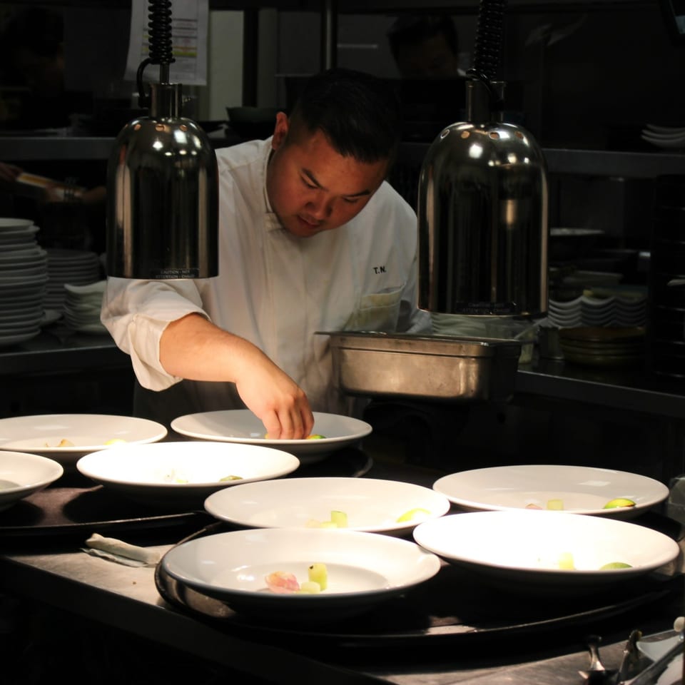 AnQi Bistro chef plating Asian-fusion dishes under heat lamps in a dark kitchen.