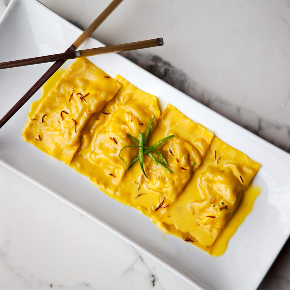 AnQi Bistro's yellow ravioli with saffron and green garnish, served on a white rectangular plate with chopsticks.