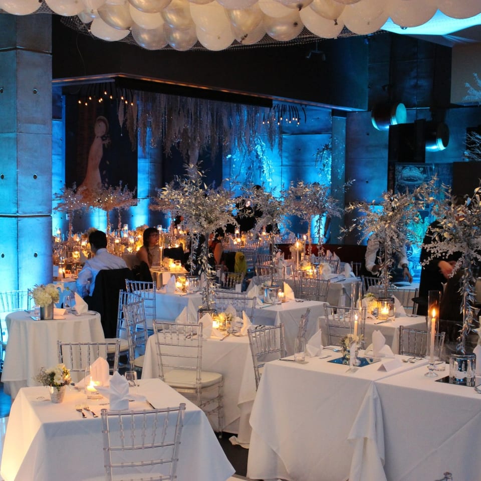 AnQi Bistro's dining room with white tablecloths, clear chairs, and silver decor under blue lighting.
