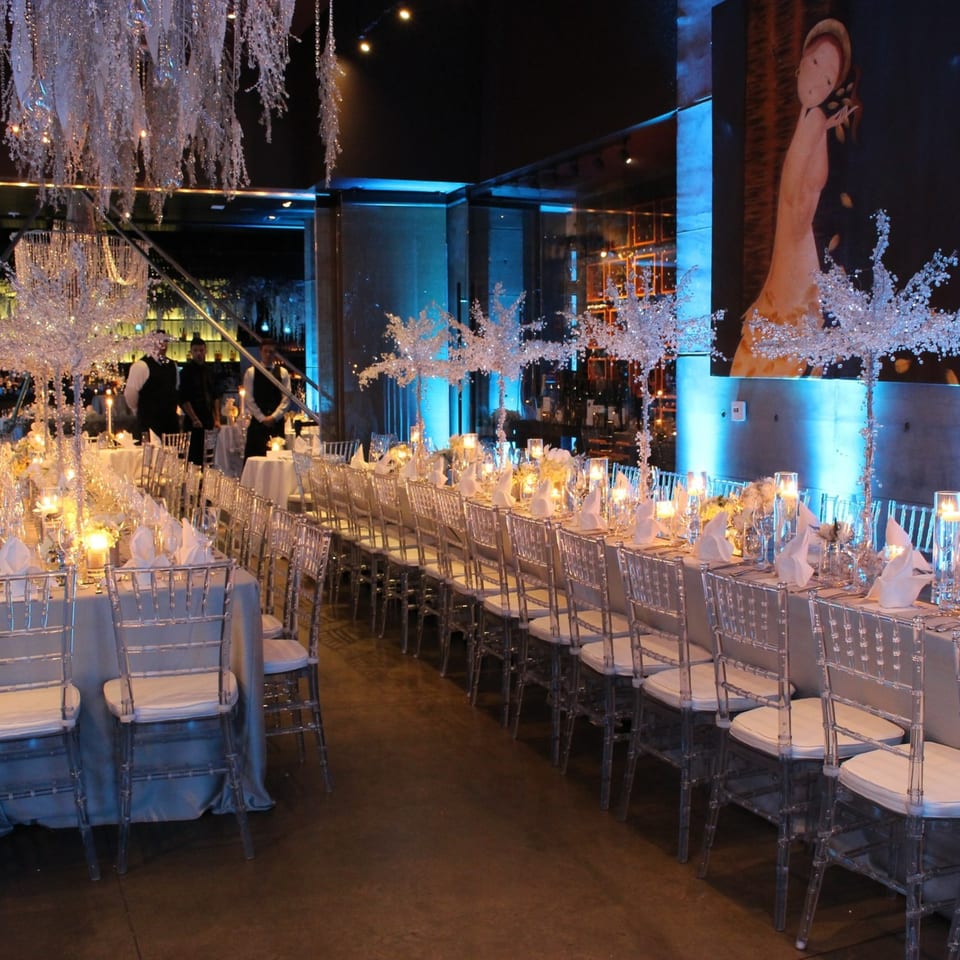 AnQi Bistro's elegant dining room with long tables set with candles, white napkins, and clear chairs.
