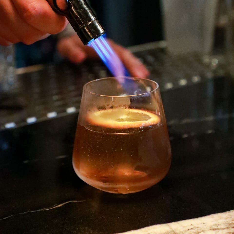Bartender torching an orange slice in a cocktail glass at AnQi Bistro.