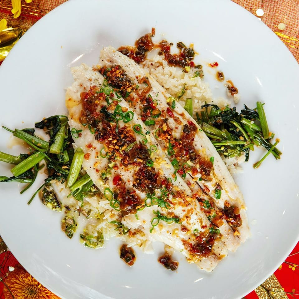 AnQi Bistro's pan-seared fish with chili garlic sauce, rice, and green vegetables on a white plate.