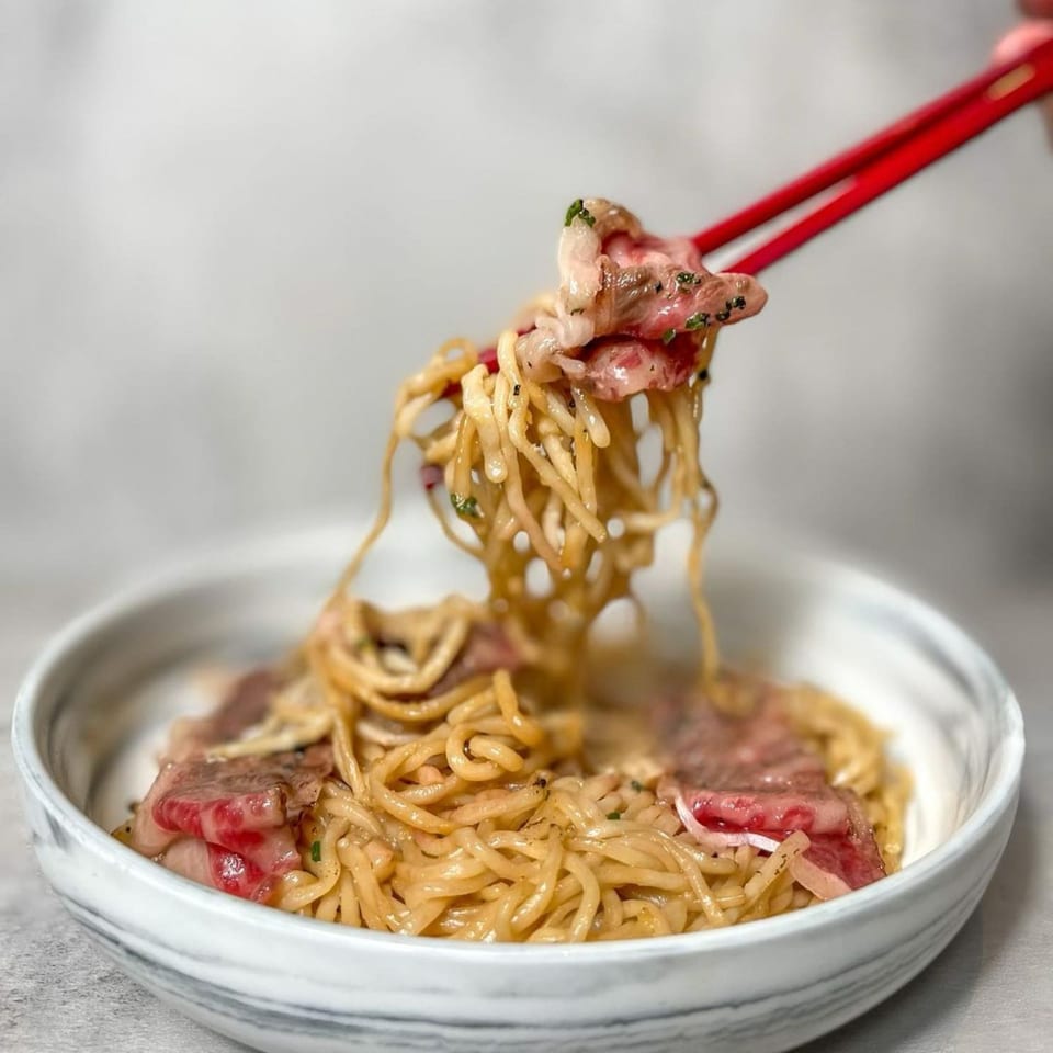 Red chopsticks lifting noodles and thinly sliced beef from a bowl of AnQi Bistro's Asian-fusion dish.