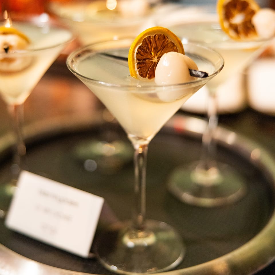 AnQi Bistro's lychee martini, garnished with a dried orange slice, on a silver tray.